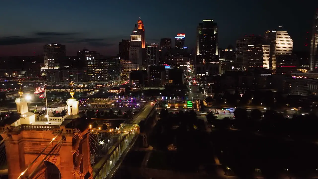 Aerial view passing the Roebling Bridge towards the illuminated Cincinnati city dusk in Ohio USA rising drone shot