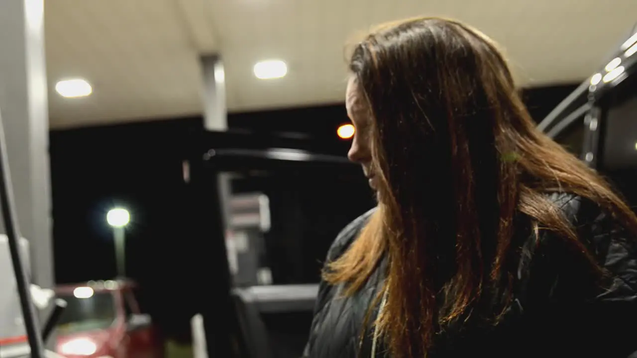 Attractive brunette waits in the cold temperatures at night by the gas pump while her vehicle is fueling up