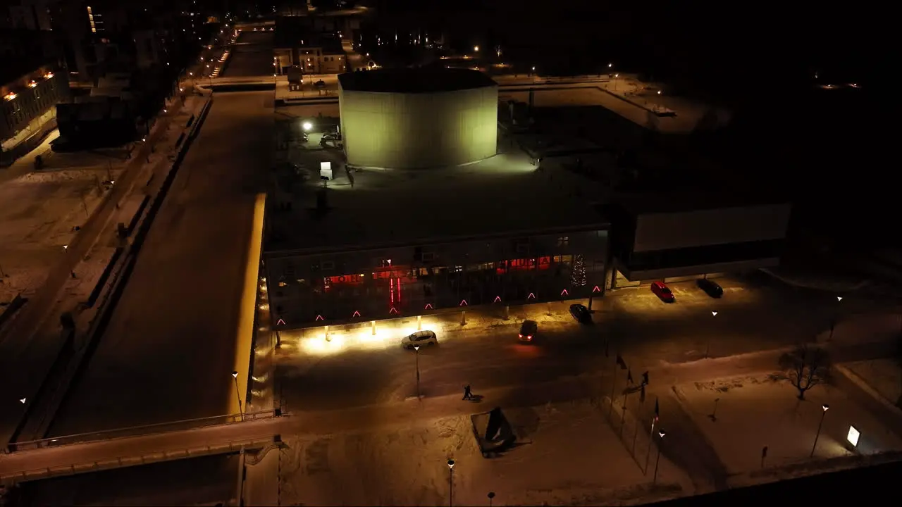 Aerial pull back away from the illuminated Oulu Theatre winter night in Finland