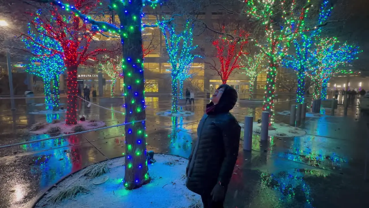 Senior woman catching snow in her mouth in a city park with Christmas lights