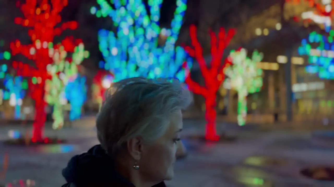 Senior woman walking in a city decorated with Christmas lights at nighttime