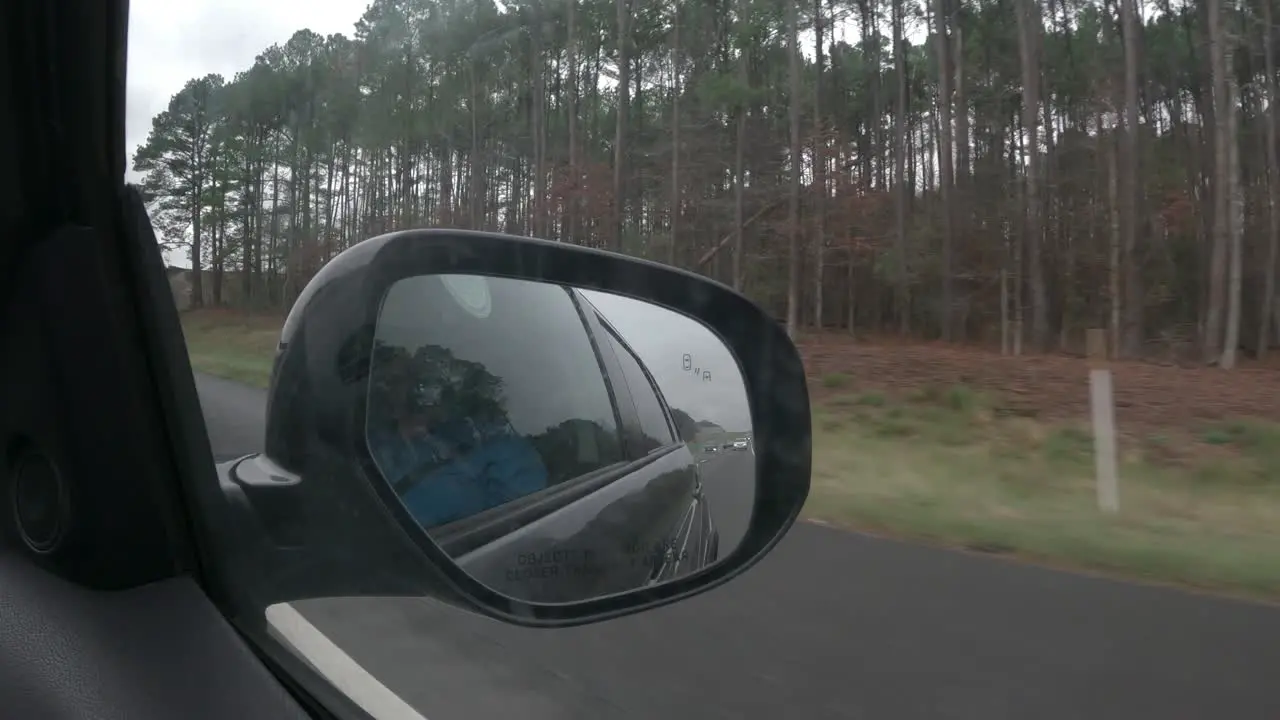 Driving along a highway passenger point of view out the side window to include the rear view mirror