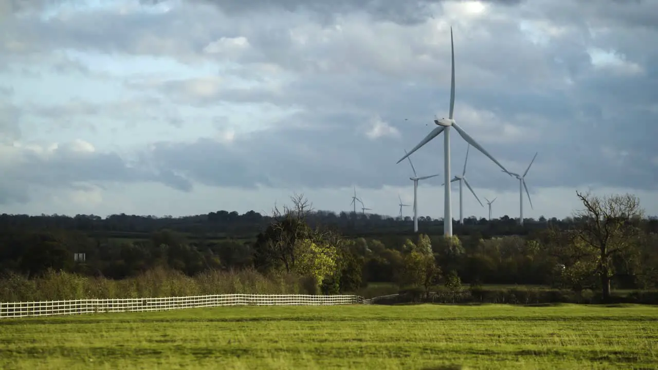 Windmills in a forested landscape wind farm on a cloudy day with field in foreground 4k