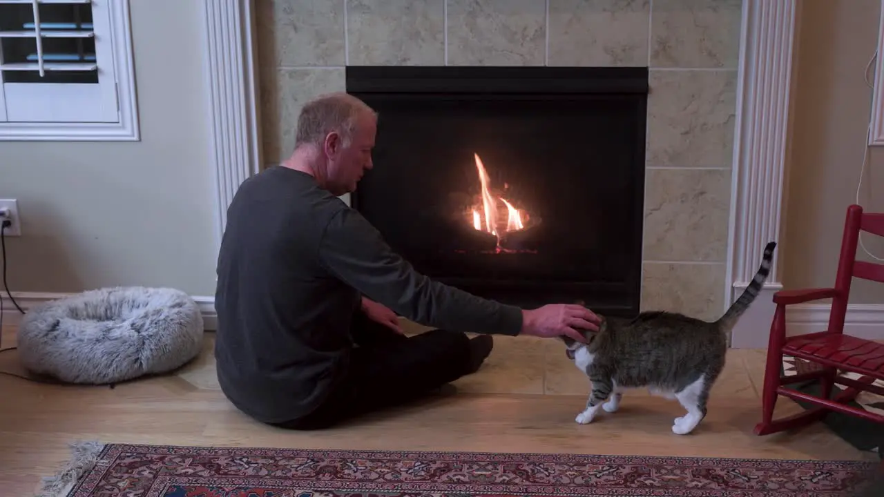 Senior man sits with his pet cat by the fireplace