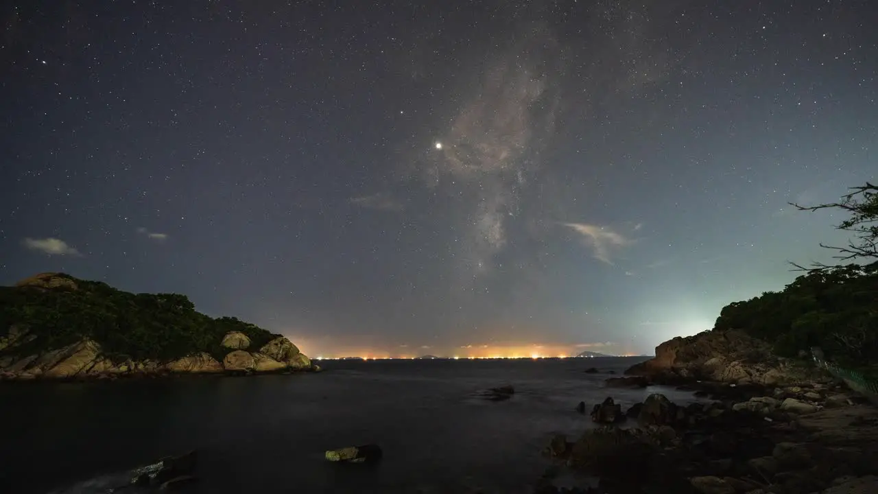 Night time illuminated Cheung Chau coastline under energetic milky way shooting star aircraft night sky timelapse