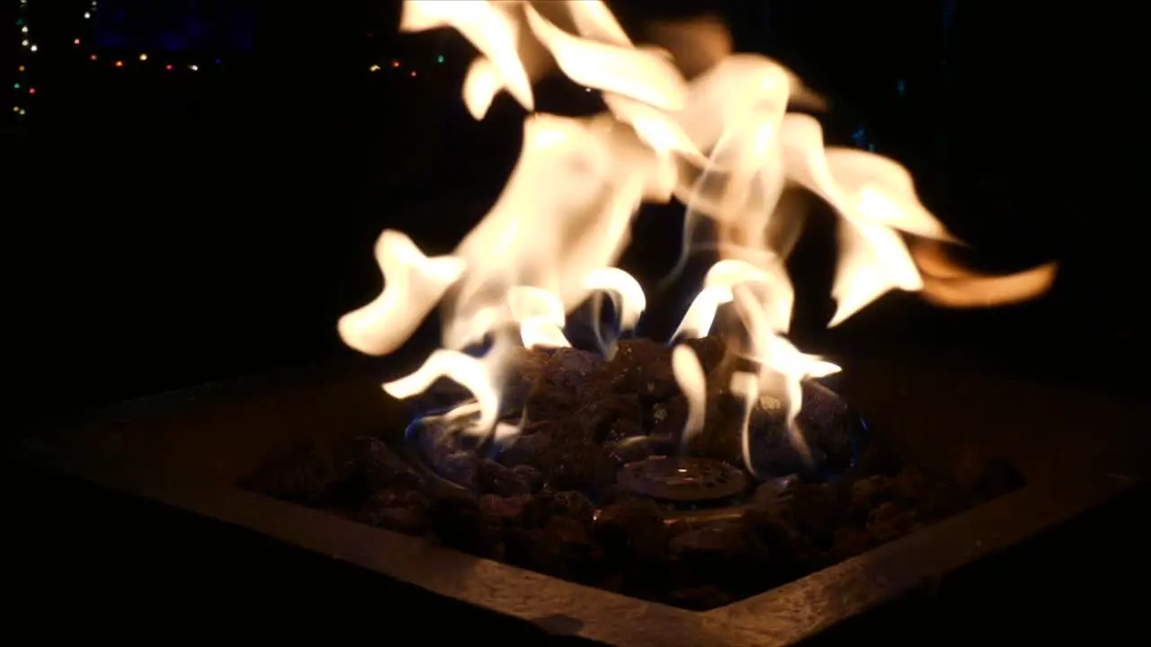 Full frame shot of outdoor fireplace burning with people walking by in the shadows in front of twinkling Christmas lights