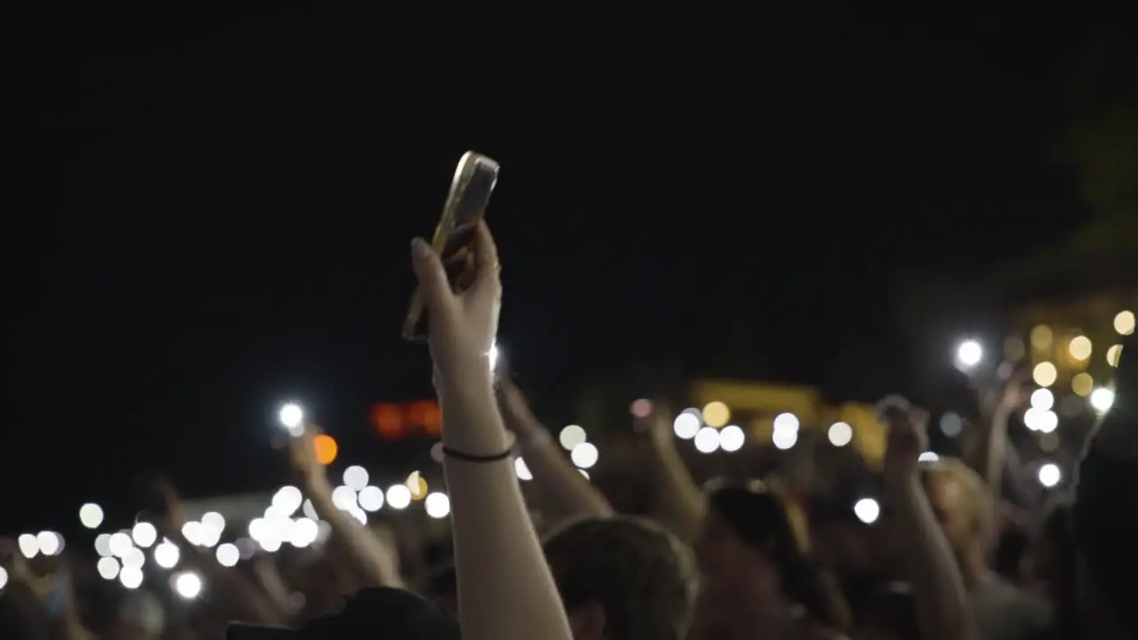 People In The Audience Waving Hands Holding Smartphones With Flashlights On