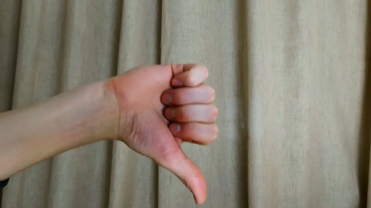 Dislike thumbs down hand symbol on a brown curtain background closeup