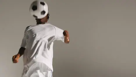 Studio Shot Of Young Male Footballer Wearing Club Kit Controlling Ball With Chest And Passing 2