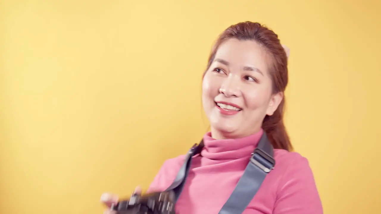 Happy delighted Asian woman with a digital camera for travel against a yellow background