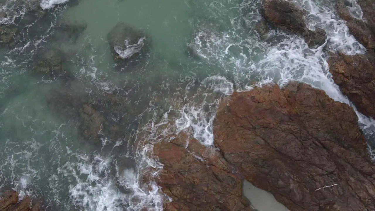 Trucking birds eye view drone shot of tropical coastline with granite rock and ocean waves and jungle