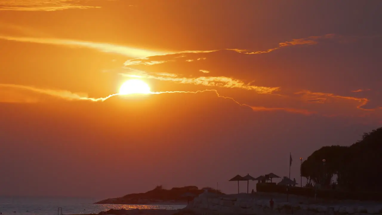 Sunset in croatia sun falling into the sea over a red orange sky silhouette of umbrellas