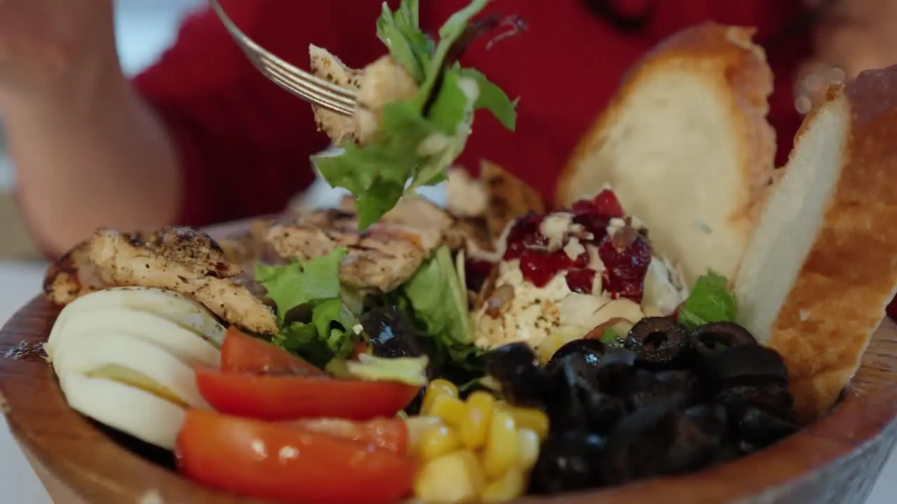 Close up side view of woman eating grilled chicken salad from wooden bowl