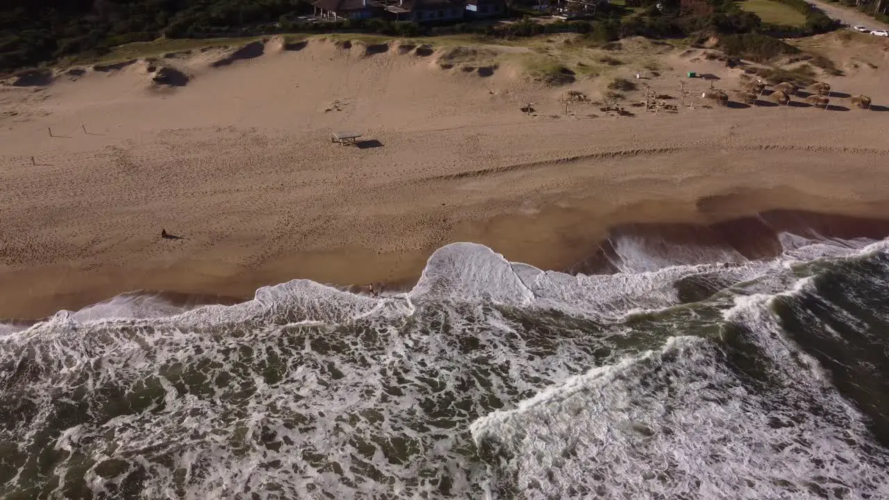 Aerial view of person entering ocean shoreline with foam during sunlight at beach Cooling in water during hot summer day in Uruguay