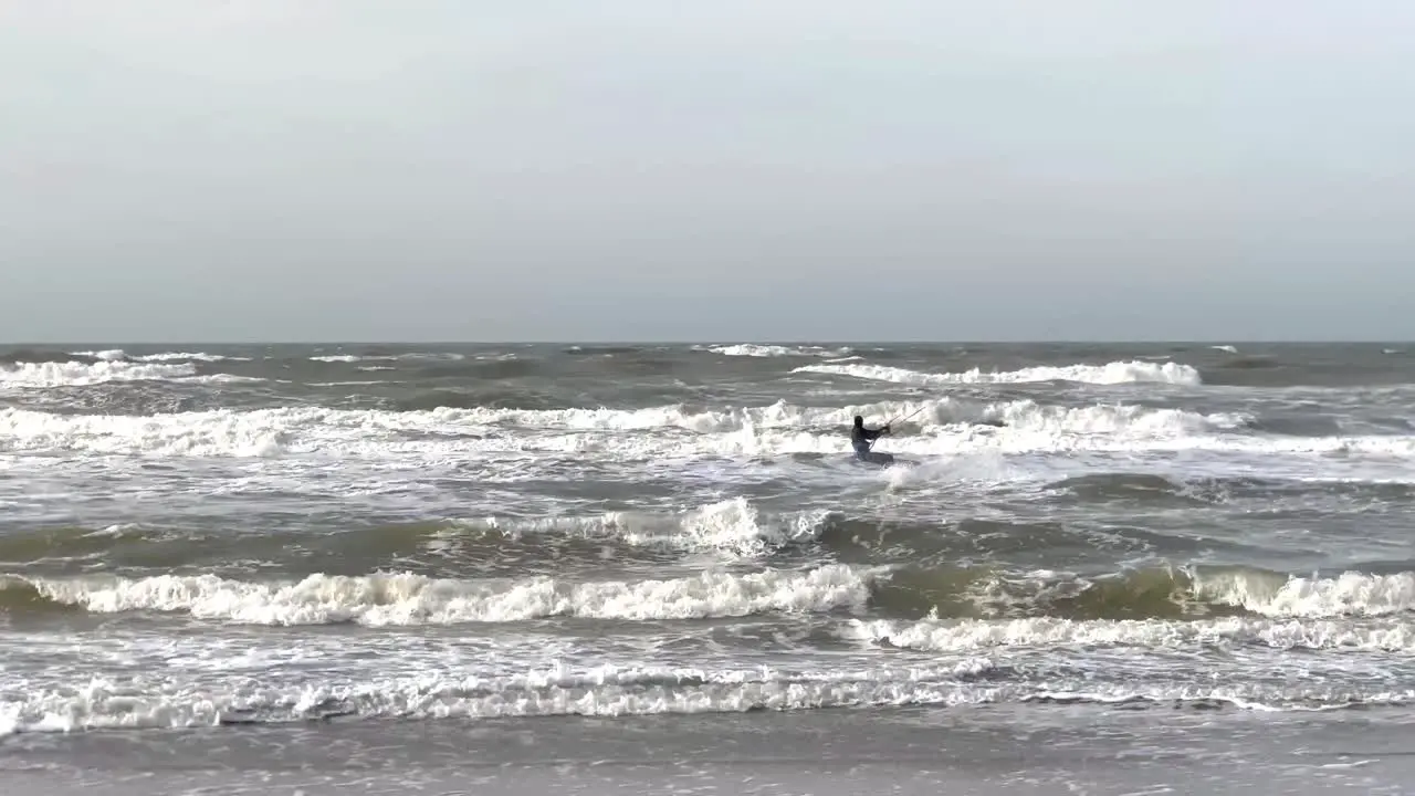 Surfer with kite jumping over large waves during cloudy day in Netherlands Wide shot