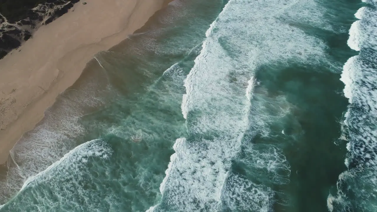 Aerial Drone follows waves as they gently roll onto pristine beach downwards shot