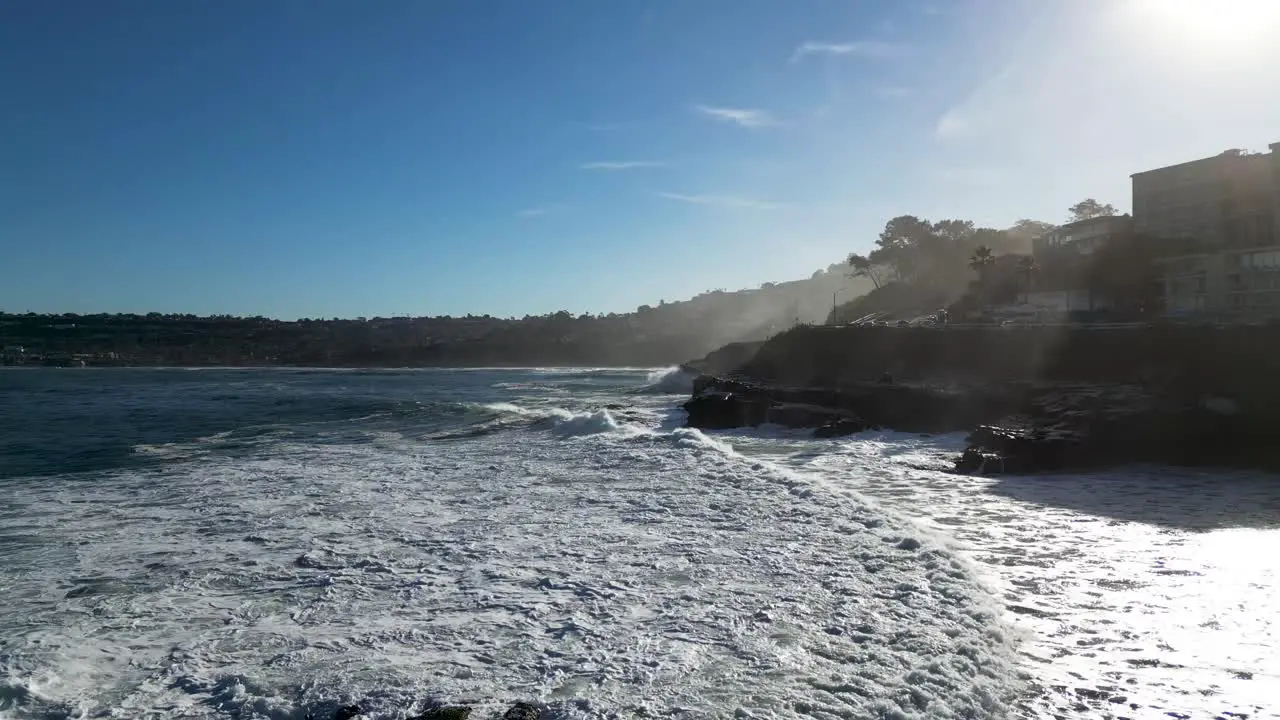 4K Footage of large ocean waves crashing on cliffs at high tide in La Jolla Cove in San Diego California as a pelican flys into shot