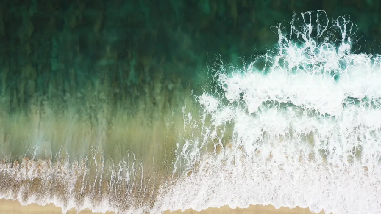 Aerial shot of the coastline of a sandy beach with gentle waves hitting the yellow sand