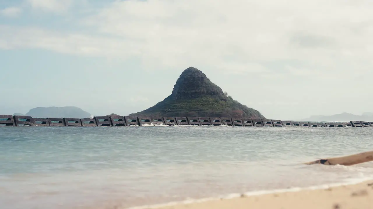 slow motion shot of Chinamans Hat Mokoli'i in Oahu Hawaii with small waves crashing on the beach in the foreground