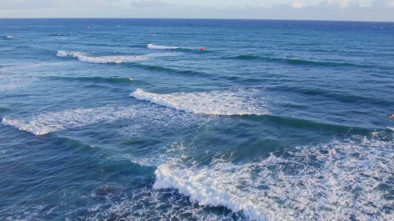 drone footage heading off shore showing the white capped ocean waves of the Blue Pacific ocean water with a spattering of surfers and kite boarders awaiting a wave near Oahu Hawaii