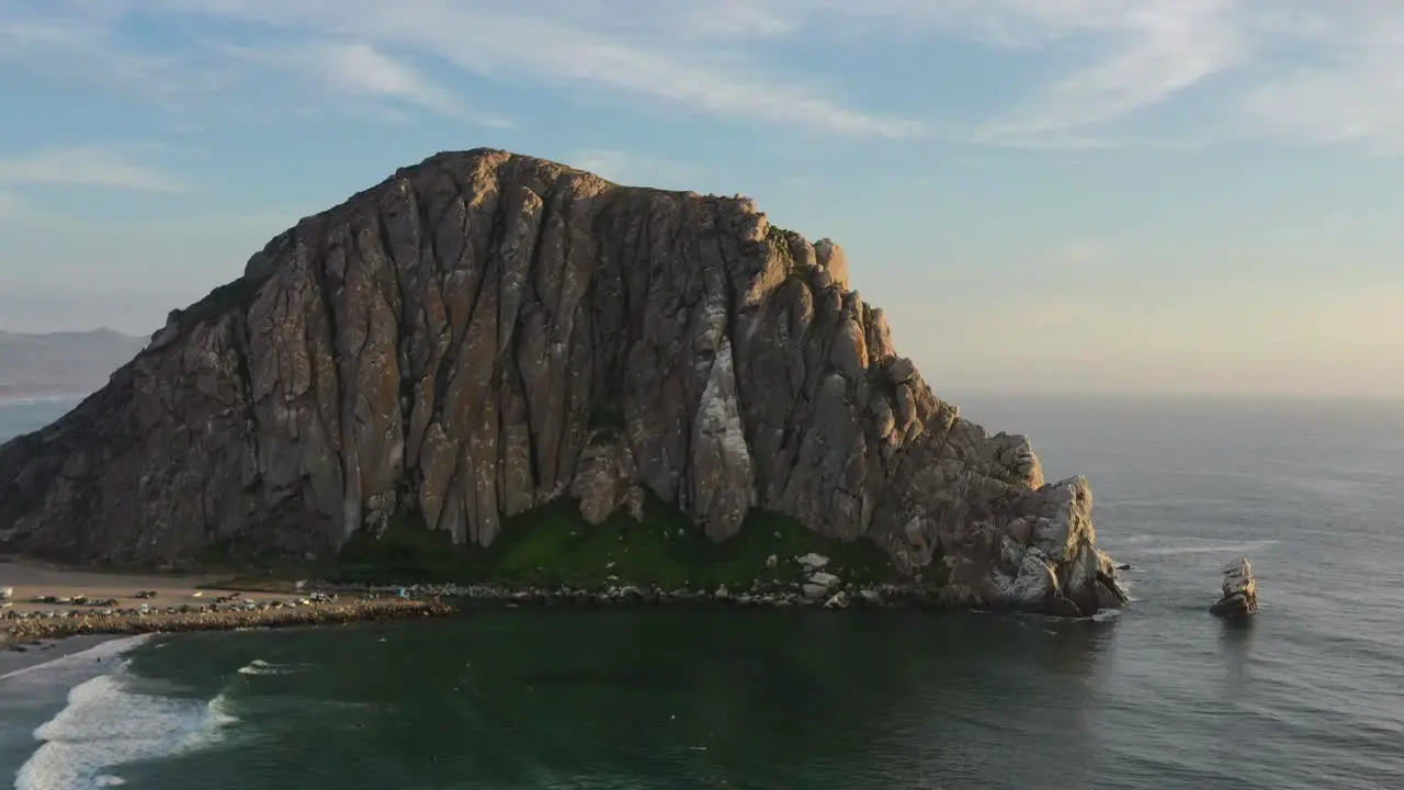 low altitude aerial drone circling Morro Bay Rock Beach during sunset in California USA as waves come crashing onto the beach