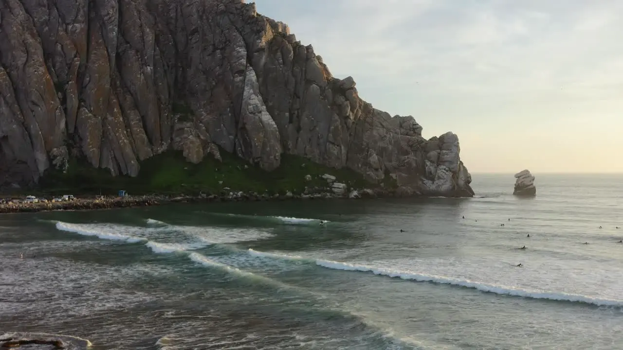 wide aerial of surfers in the ocean trying to catch waves in the Pacific Ocean at Morro Bay Rock Beach in California USA during sunset