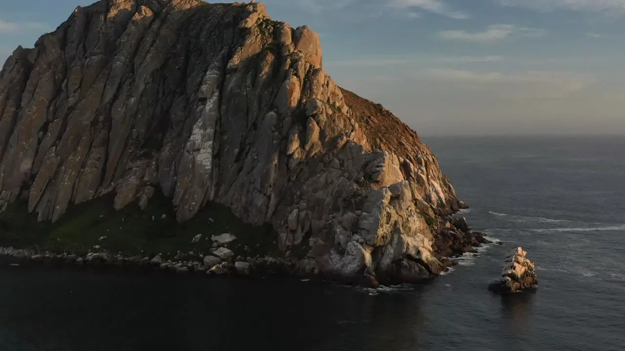 aerial drone panning around a unique rock formation on an island during sunset as the sun reflects off the rock in Morro Bay California