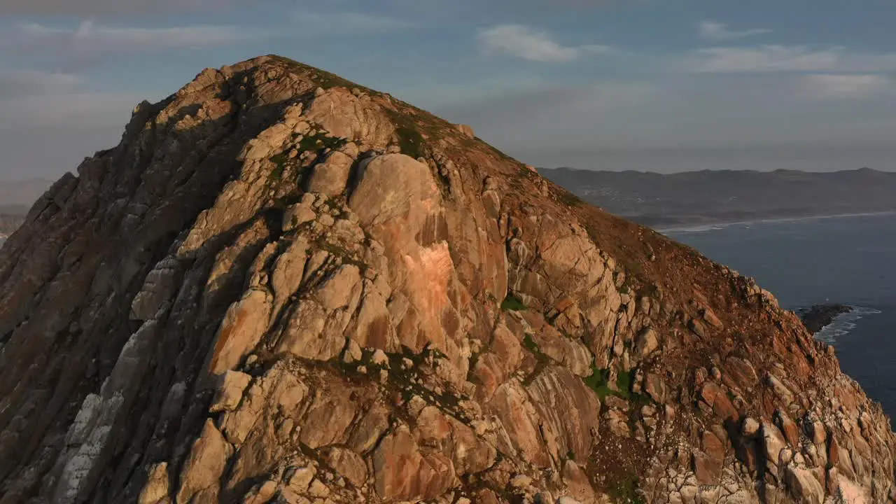 aerial drone panning above Morro Bay Rock during sunset revealing the bay behind and a fishing boat anchored in the harbor