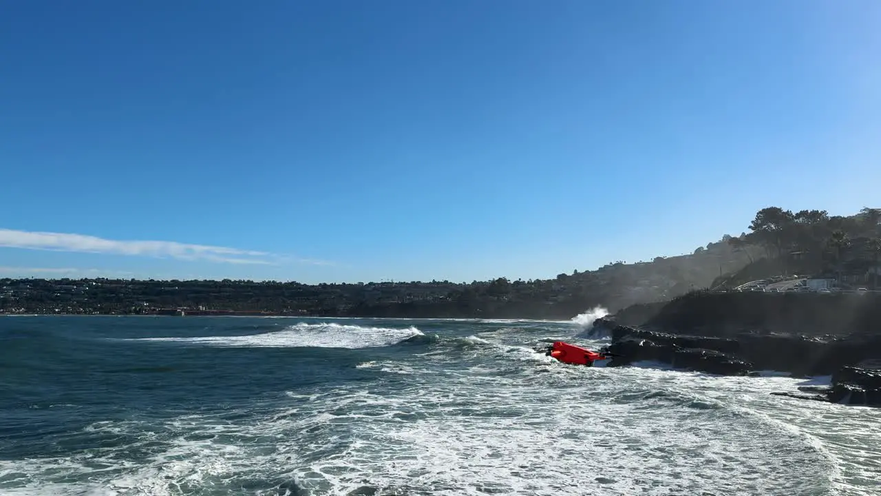 4K footage of drone flying from right to left into and out of shot with large ocean waves crashing on cliffs during high tide in La Jolla Cove San Diego California