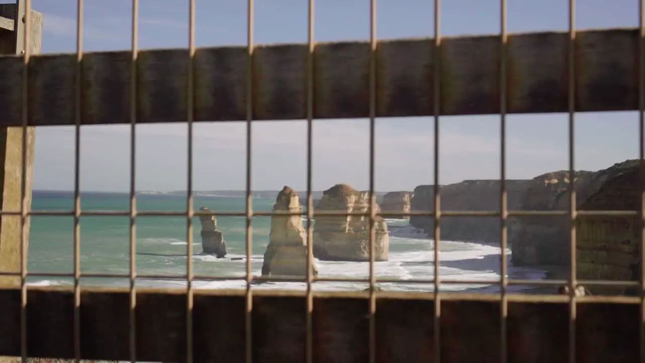 Waves lapping against Twelve Apostles through a caged fence point of view