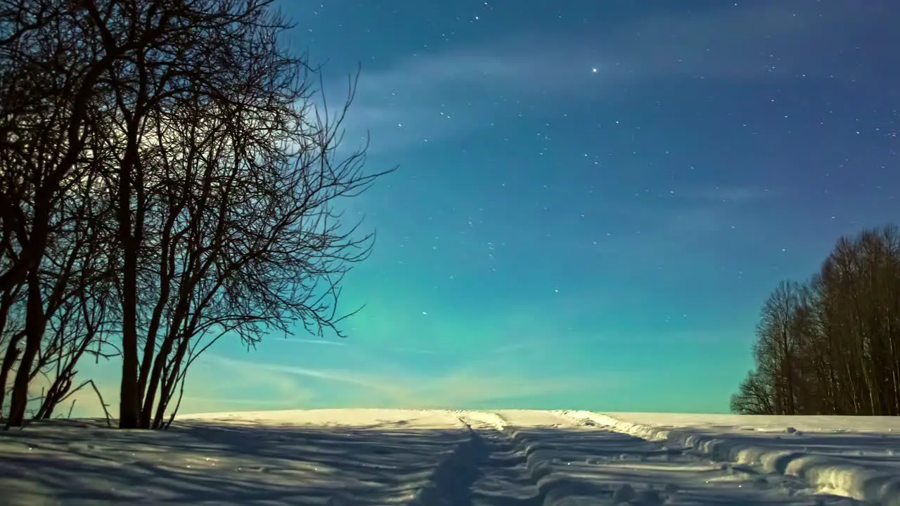 The Northern lights or aurora borealis dancing just above the horizon on a starry night with the moon setting in a winter wonderland time lapse