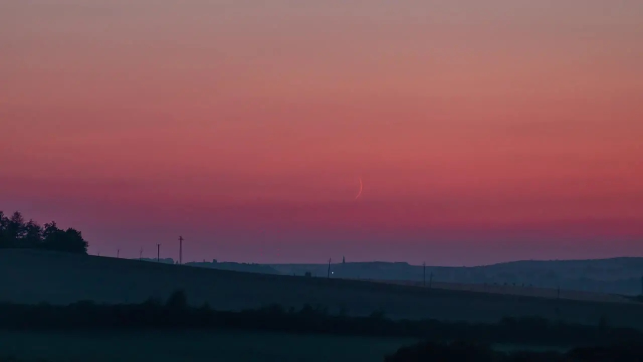 Crescent moon set time lapse with orange sky and short fireworks on the horizon less surroundings