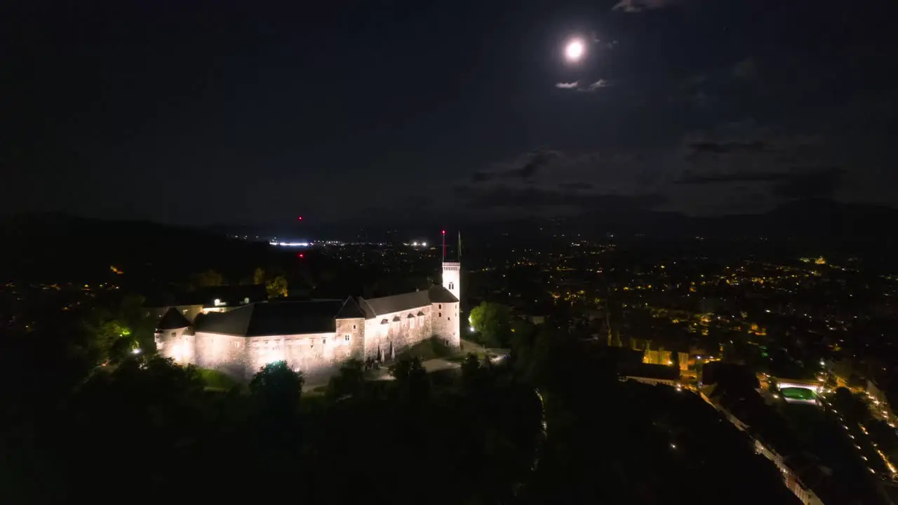 Night aerial hyperlapse of Ljubljana castle flying under full moon moonlight city lights drone