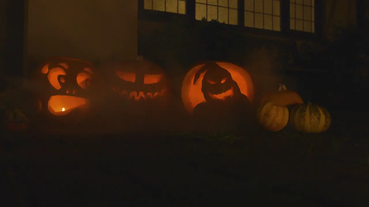 3 carved lit pumpkins outside the front of a house Halloween with smoke slow motion