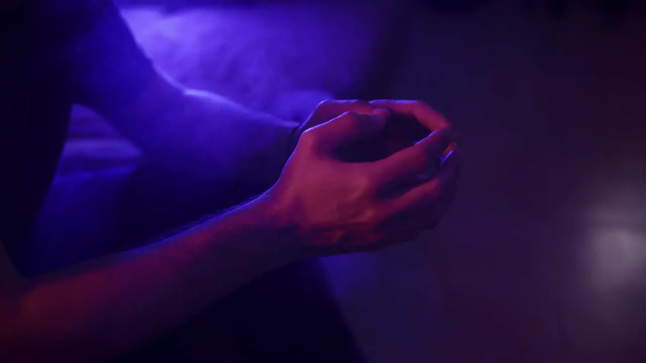 Static shot of a man tapping his fingers together surrounded by smoke in vibrant lighting