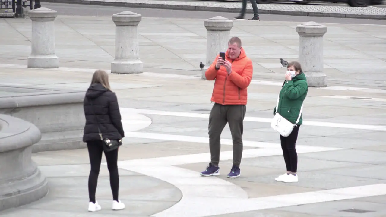 A group of tourists take turns to have their photos taken in Trafalgar Square the one wearing a surgical face mask removes it to have her photo taken