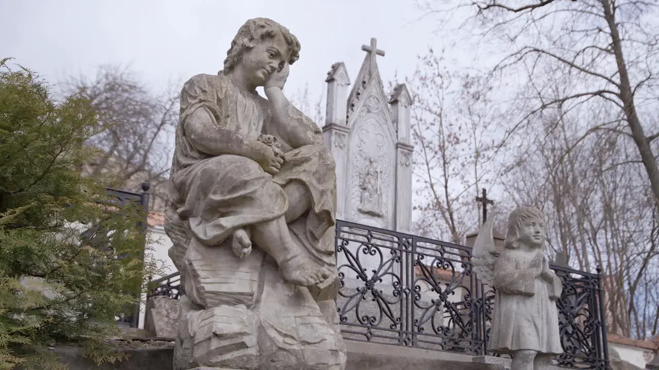 Two Stone Statues in Graveyard in Front of Big Tombstone in Uzupis Cemetery