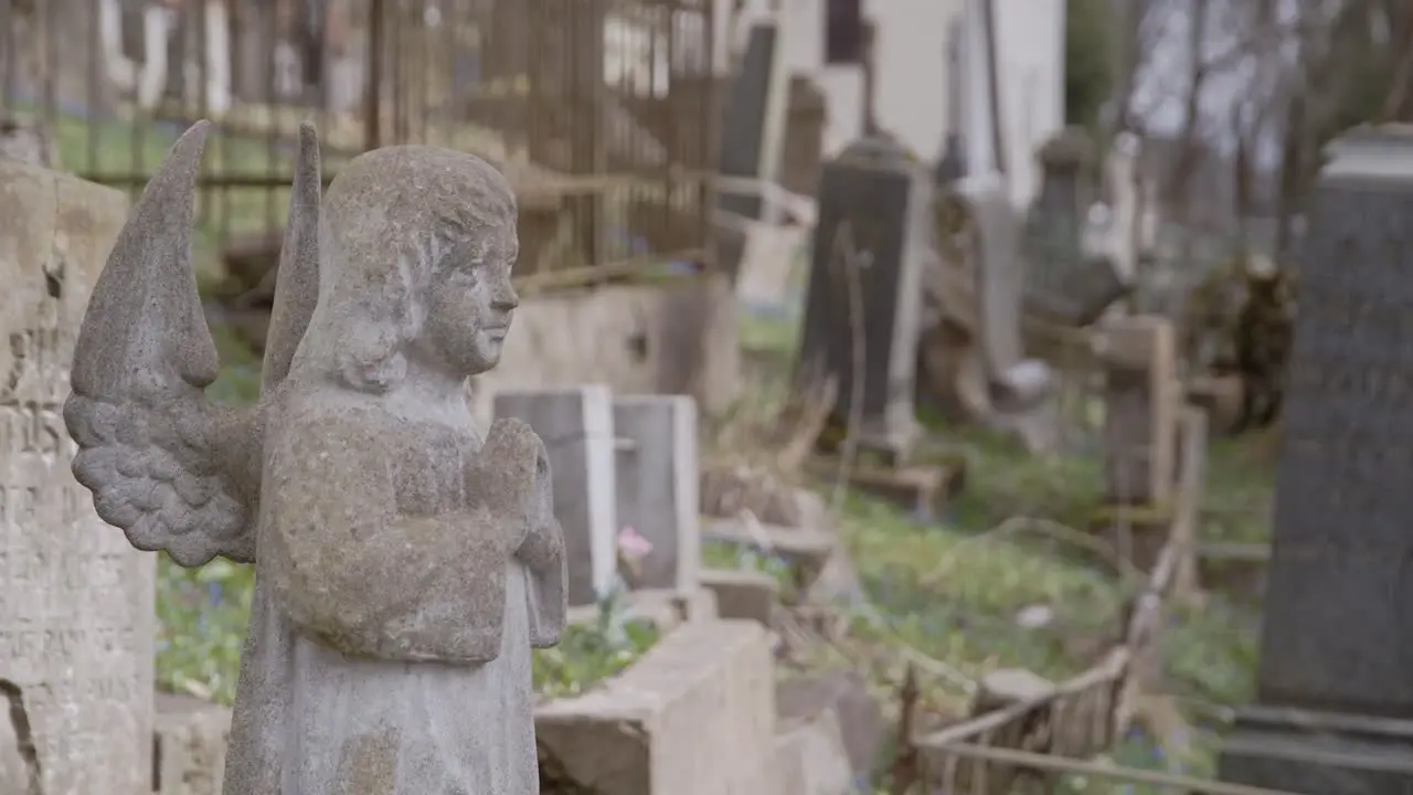 Little Cute Stone Angel Praying in front of Tombstone with Graveyard in Background