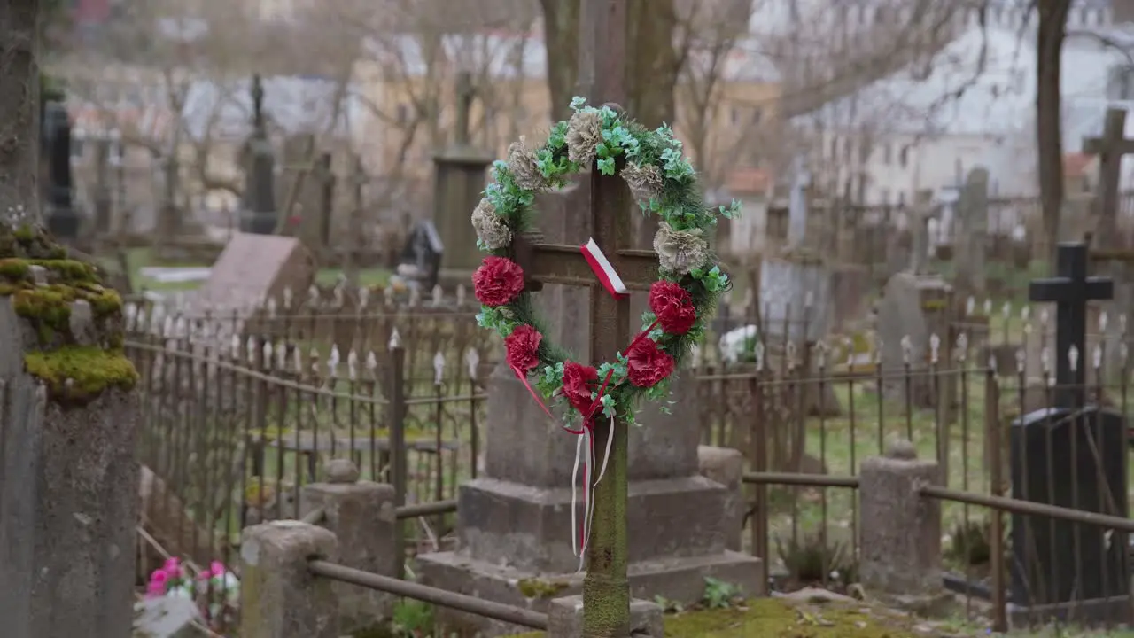 Old Rusty Metal Cross with Artificial Flower Wreath and Ribbon Polish Flag in Old Graveyard