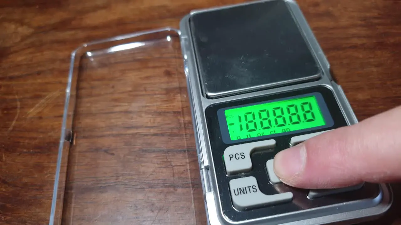 Pocket digital LCD precise scale in grams and ounces measuring and weighing with finger pressing the on button and green display appears at zero tare