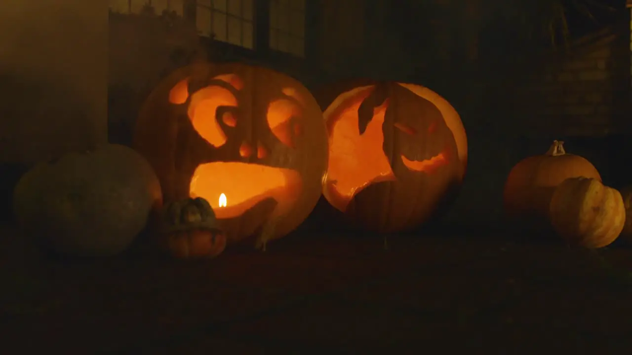 2 carved lit pumpkin outside the front of a house Halloween with smoke with little pumpkins