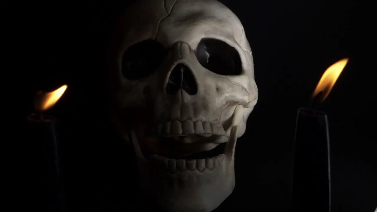 Human skull closing mouth between two candles on dark background