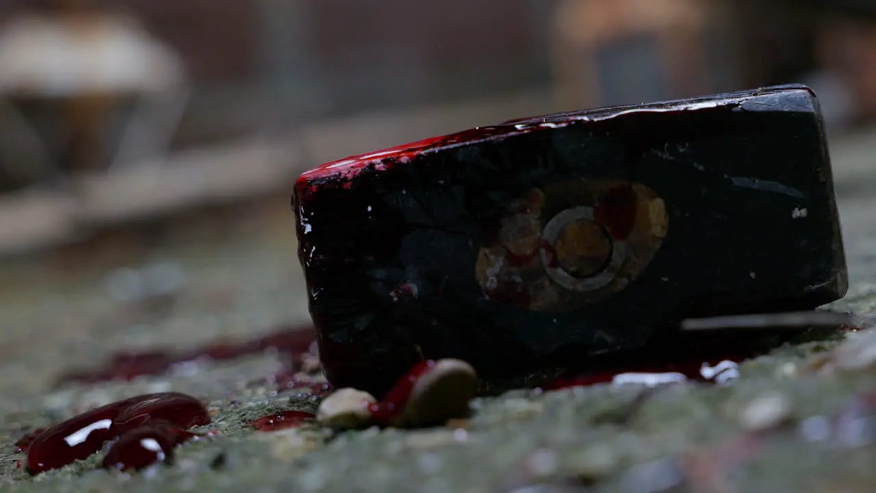 Close up of a bloody lump hammer as a light swings overhead and casts shadows onto the grimy concrete floor