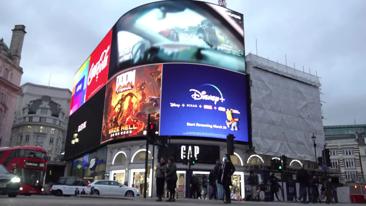 A woman wearing a surgical face mask walks across a pedestrian crossing and past the neon advertisement billboard sign at Piccadilly Circus