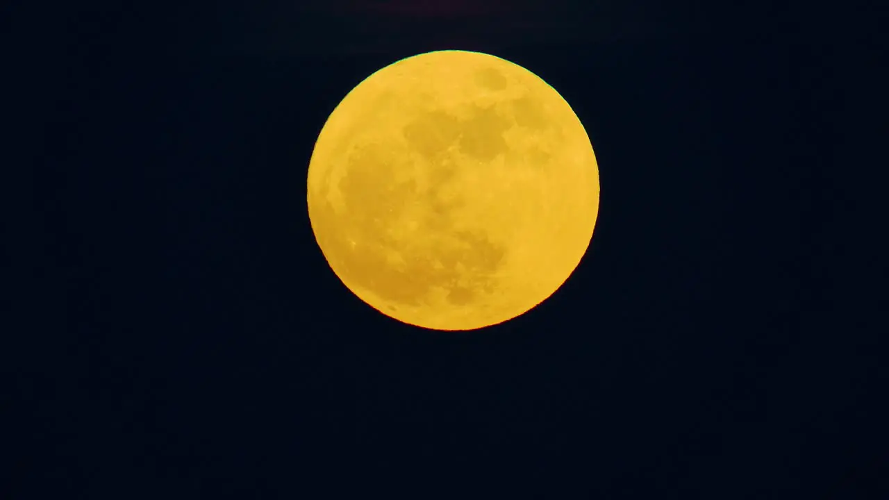 Orange yellow gradient tinted full blue supermoon moon against dark black sky gentle glow