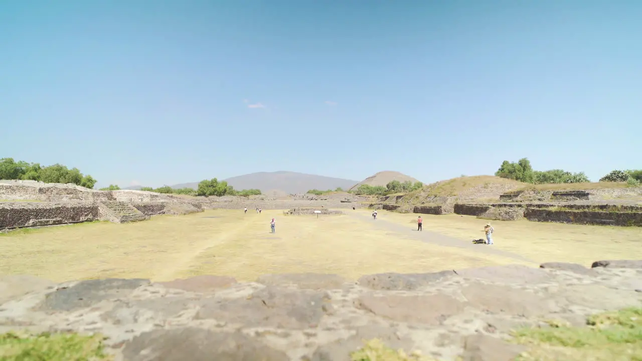 Wide shot of pre-Columbian Teotihuacan Pyramids site in Mexico with tourists in the distance on a sunny day