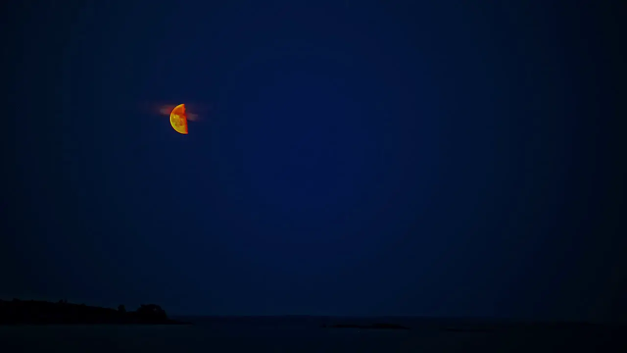 Timelapse on a clear blue night of half moon going up the night sky over the sea coast