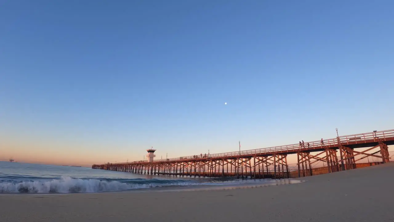 The moon setting over the beach with a long wooden pier at sunrise seascape time lapse