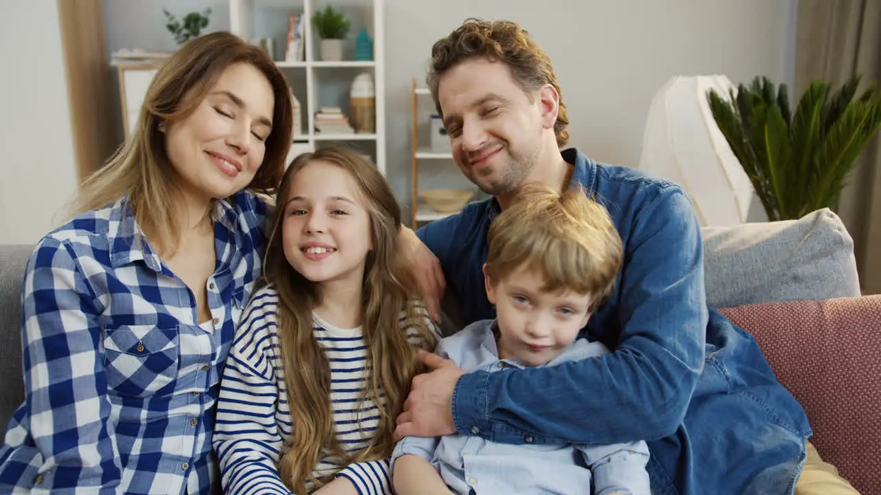 Happy Smiled Family Sitting On The Sofa In The Living Room And Smiling To The Camera