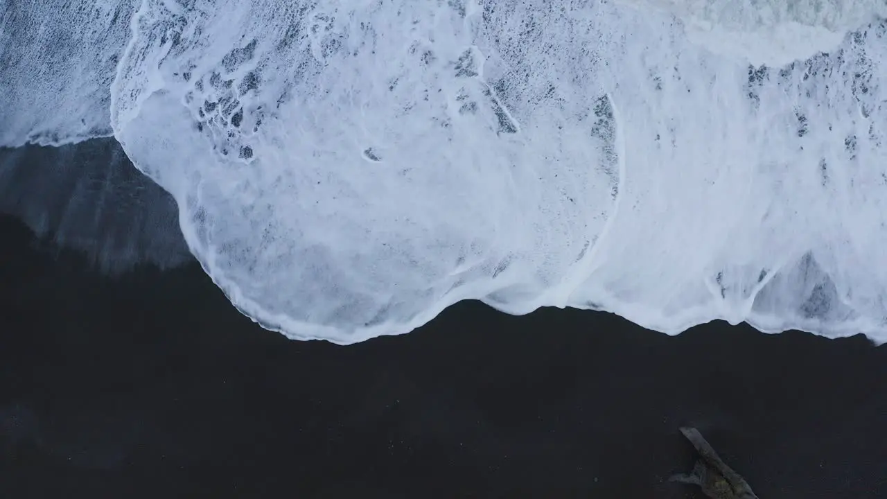 Aerial top down shot of foamy waves reaching black sandy beach in Iceland